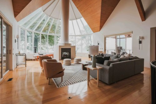 Spacious modern living room with large windows, a fireplace, and stylish furniture, featuring wooden accents and a cozy atmosphere.