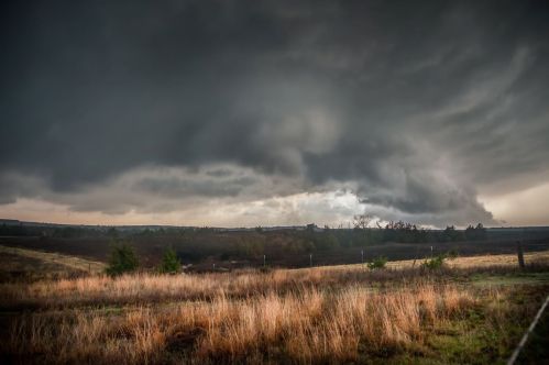 Dark, ominous clouds loom over a grassy field, hinting at an approaching storm in the distance.