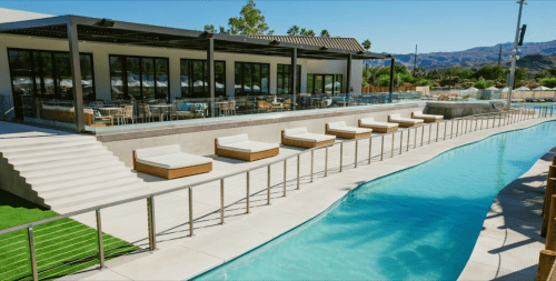 A modern pool area with lounge chairs, steps leading to a restaurant, and scenic views of hills in the background.