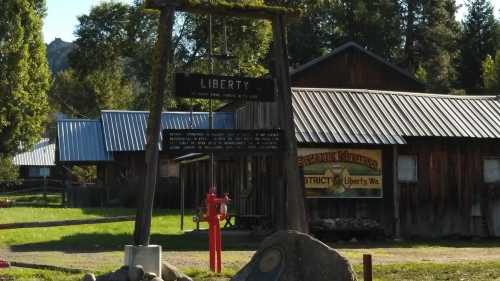 A wooden sign reading "LIBERTY" stands in front of rustic buildings in a green landscape.