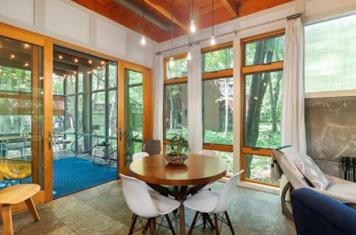 Bright, modern sunroom with a round table, white chairs, and large windows overlooking a green outdoor space.