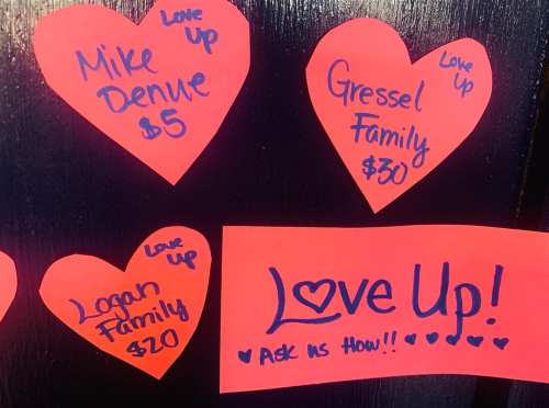 Colorful heart-shaped notes with names and donation amounts, promoting a "Love Up!" initiative.