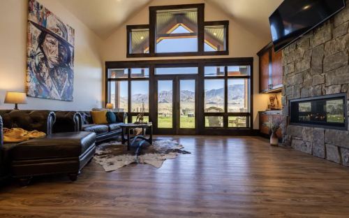 Cozy living room with large windows, mountain views, a stone fireplace, and stylish furniture.