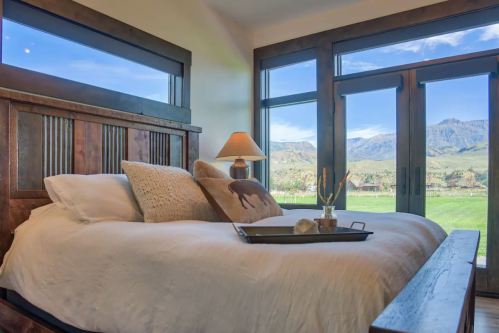 Cozy bedroom with a wooden bed, decorative pillows, and large windows showcasing a scenic mountain view.