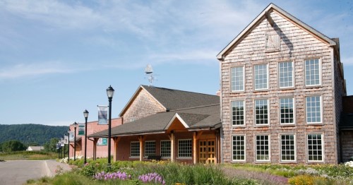 A large, rustic building with wooden shingles and multiple windows, surrounded by flowers and lampposts under a blue sky.