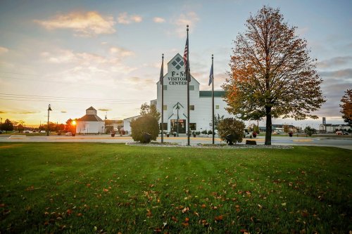 Sunset over the F-M Visitor Center, surrounded by trees and flags, with autumn leaves on the grass.