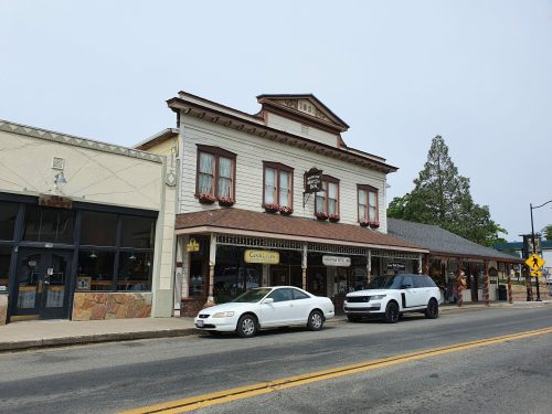 Historic building with flower boxes, shops below, and parked cars on a quiet street under a cloudy sky.