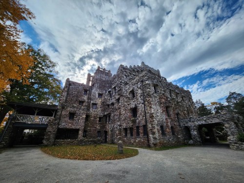 A historic stone castle with a rugged exterior, surrounded by trees and a cloudy sky.