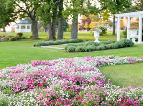 A vibrant garden with colorful flower beds, green lawns, and decorative structures in the background.