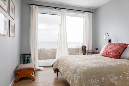 Cozy bedroom with a bed, decorative pillows, and large window overlooking a serene outdoor view.