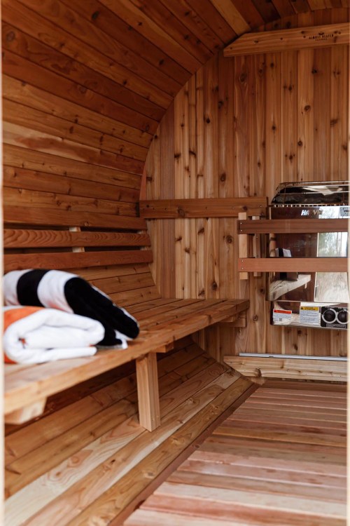 Interior of a wooden sauna featuring benches, neatly stacked towels, and a stove, all in warm, natural tones.