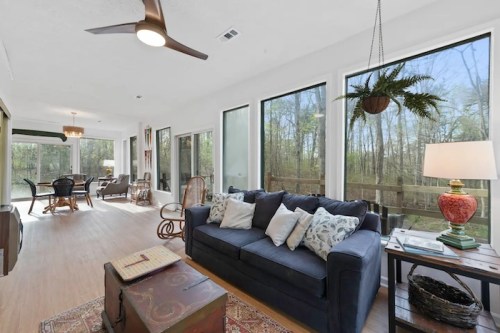 Bright living room with large windows, a navy sofa, decorative pillows, and a view of a wooded area outside.