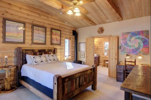Cozy wooden bedroom with a large bed, art on the walls, and a door leading to a bathroom. Warm, inviting atmosphere.