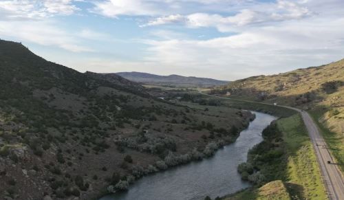 A winding river flows through a green valley surrounded by hills under a partly cloudy sky.