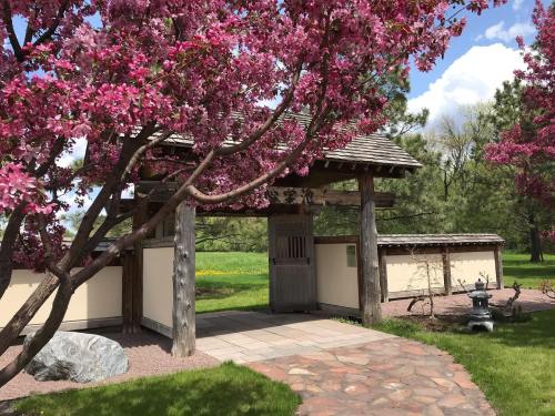 A serene garden entrance framed by blooming pink trees and a stone pathway leading to a traditional structure.