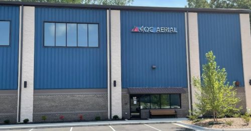 Exterior of a blue and white building with the sign "KOC AERIAL" and landscaped parking area in front.