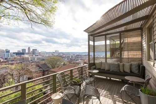 A modern balcony with seating overlooks a city skyline under a partly cloudy sky.