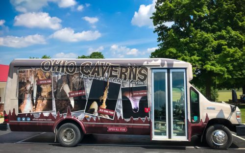 A bus wrapped in promotional graphics for Ohio Caverns, featuring cave images and the text "Open All Year."