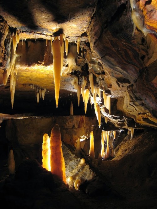 Stalactites and stalagmites illuminated in a dark cave, showcasing unique rock formations and textures.