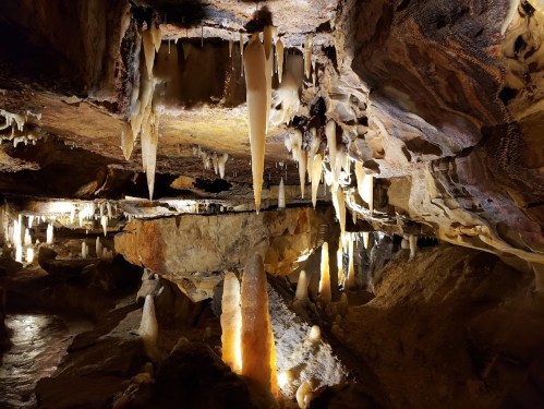 Stalactites and stalagmites illuminated in a dark cave, showcasing unique rock formations and textures.