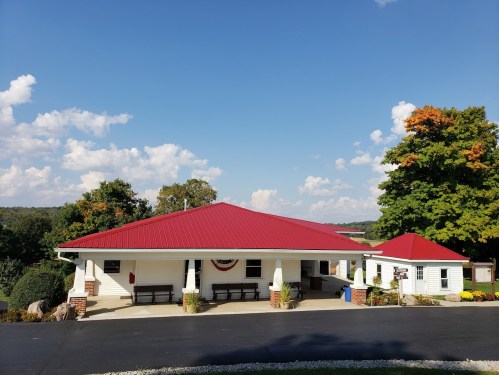 A one-story building with a red roof, surrounded by trees and a clear blue sky, featuring a welcoming entrance.