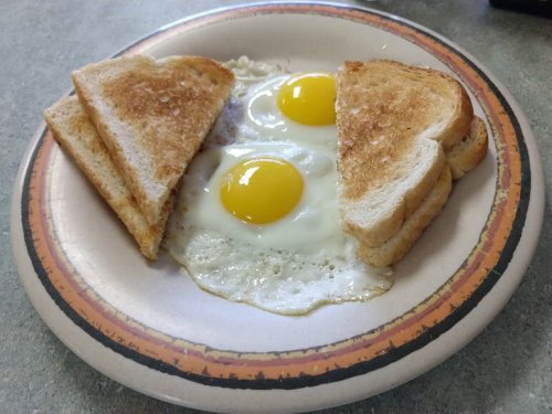 A plate with two fried eggs and two slices of toasted bread arranged around them.