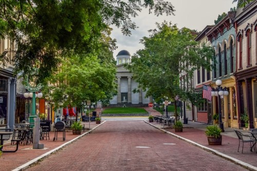 A quiet street lined with trees and historic buildings, leading to a distant dome-topped structure.