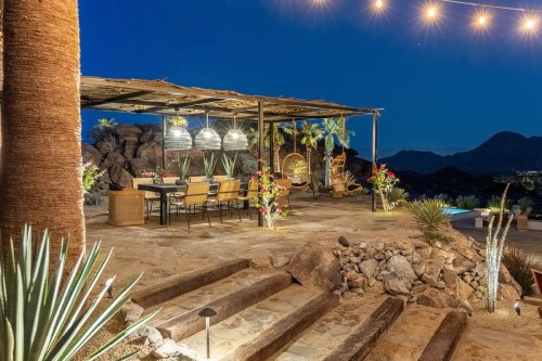 Outdoor dining area with string lights, surrounded by plants and rocks, set against a night sky.