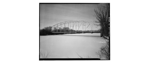 A black and white photo of a bridge spanning a frozen river, surrounded by bare trees and a clear sky.