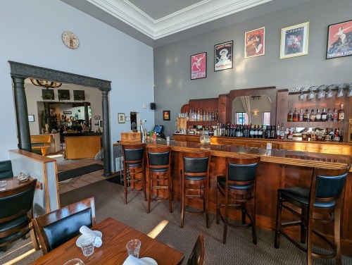 A cozy bar area with wooden furniture, a mirrored back bar, and framed posters on the walls in a warm, inviting setting.