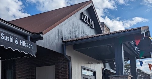 Exterior of a restaurant named "Izumi," featuring a roof and colorful flags, with signs for sushi and hibachi.