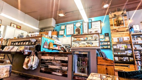 Cozy café interior featuring a wooden counter, display case, shelves of products, and colorful wall decor.