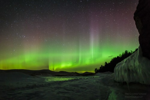 A stunning night sky illuminated by vibrant green and purple auroras over a snowy landscape.