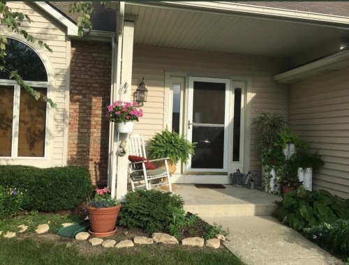 A welcoming front porch with a rocking chair, potted plants, and a decorative entrance.