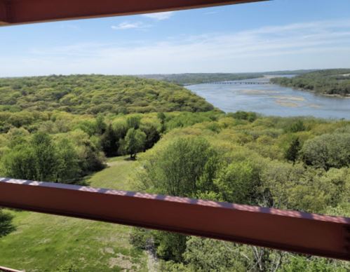 A scenic view of lush green hills and a river, framed by a structure's railing under a clear blue sky.