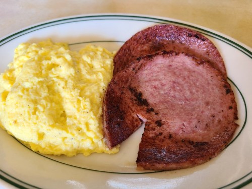 A plate with fluffy scrambled eggs and two slices of browned, grilled bologna.