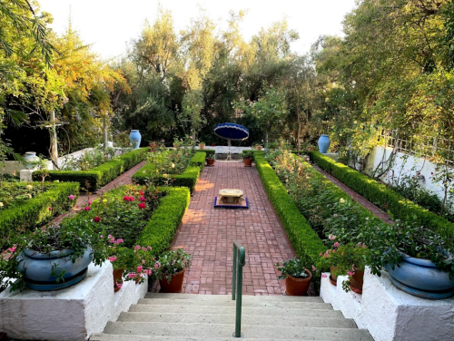 A serene garden with neatly trimmed hedges, colorful flowers, and a central fountain, surrounded by lush greenery.