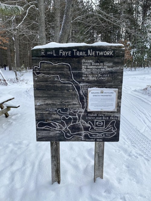 A snowy trail sign for the R and L Frye Trail Network, detailing rules and a map of the area.
