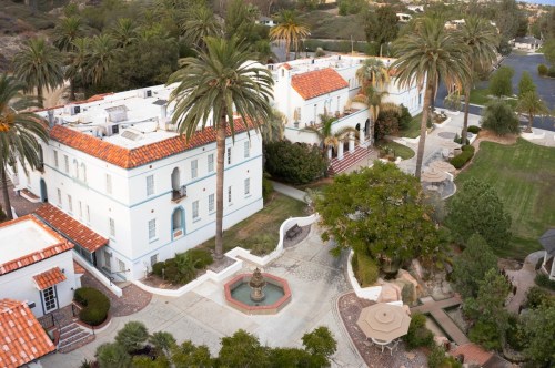 Aerial view of a Mediterranean-style estate with palm trees, a fountain, and landscaped gardens.