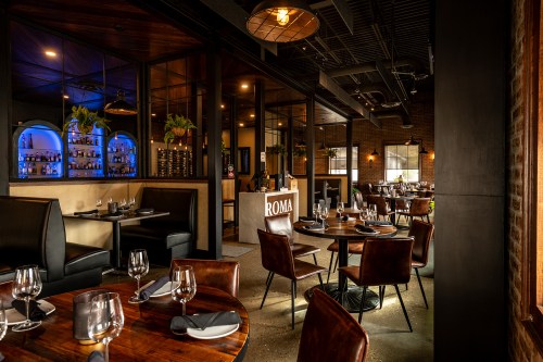 A modern restaurant interior featuring elegant tables, leather chairs, and a stylish bar area with ambient lighting.