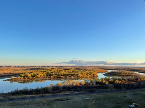 A serene landscape featuring a winding river surrounded by trees and open fields under a clear blue sky.