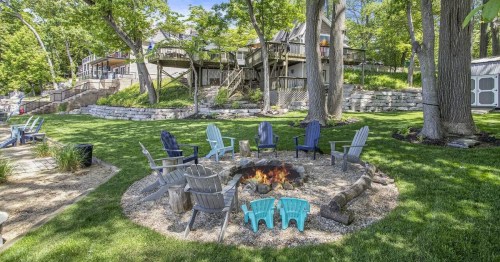 A cozy fire pit surrounded by colorful chairs in a lush green yard, with houses and trees in the background.