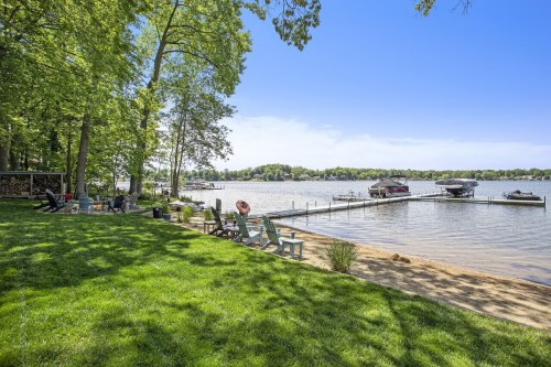 A serene lakeside view with green grass, boats docked, and trees lining the shore under a clear blue sky.