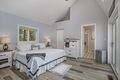 Bright, modern bedroom with a large bed, light blue walls, and an adjoining bathroom. Natural light from windows.