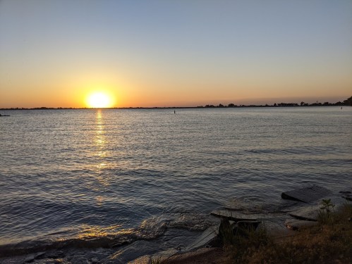 A serene sunset over a calm lake, with gentle waves lapping at the shore and a clear sky.