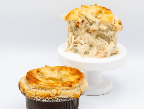 A golden-brown chicken pot pie on a pedestal, with a slice revealing creamy filling and vegetables inside.