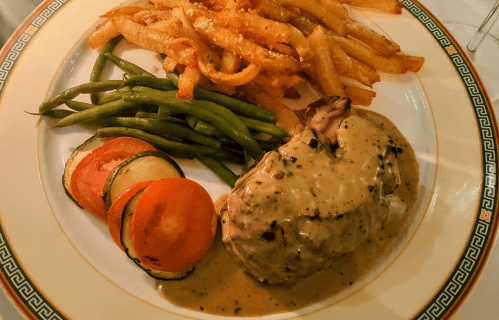 A plate featuring a meat dish with creamy sauce, green beans, sliced vegetables, and crispy French fries.