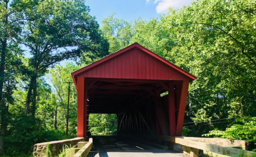 A red covered bridge surrounded by lush green trees under a clear blue sky.