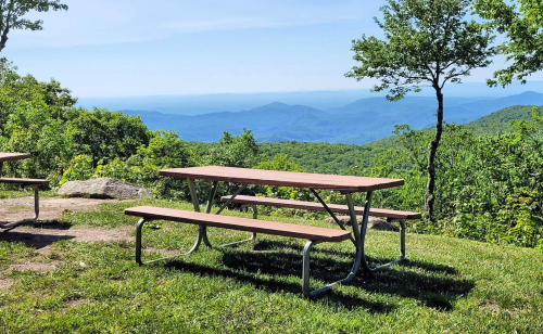 A picnic table on a grassy area overlooking a scenic mountain view under a clear blue sky.