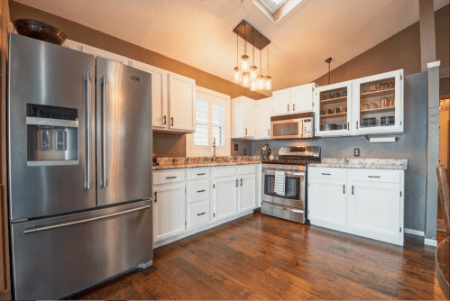 Modern kitchen with stainless steel appliances, white cabinets, granite countertops, and wooden flooring. Bright and spacious.